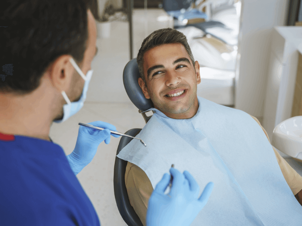 guy sitting in a dental chair smiling at dentist